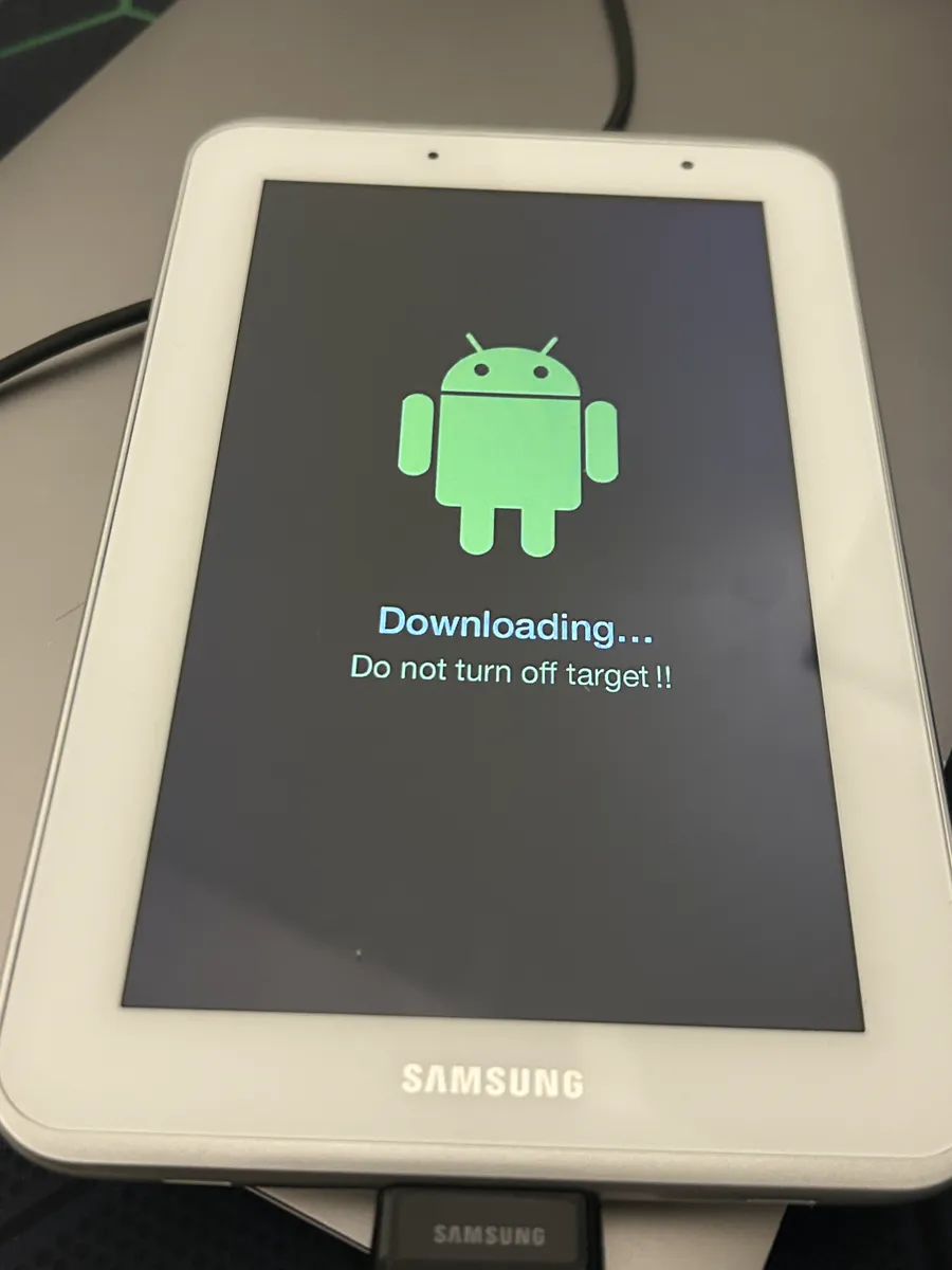 La Galaxy Tab 2 blanca, conectada por USB, con la pantalla «Downloading… Do not turn off target !!» bajo el robot verde de Android