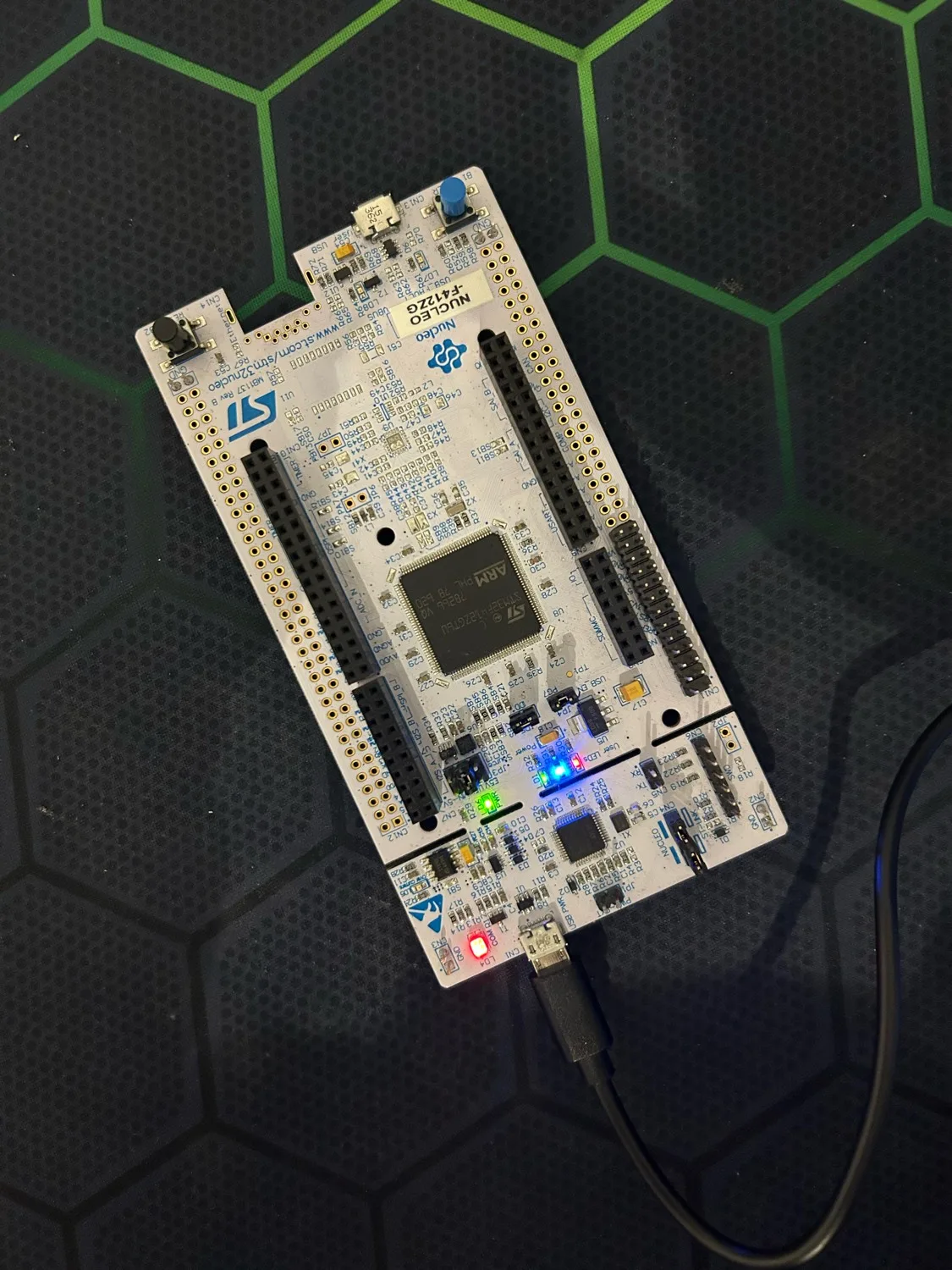 La carte NUCLEO-F412ZG posée sur un tapis noir, branchée en USB, avec ses LEDs utilisateur verte, bleue et rouge allumées.